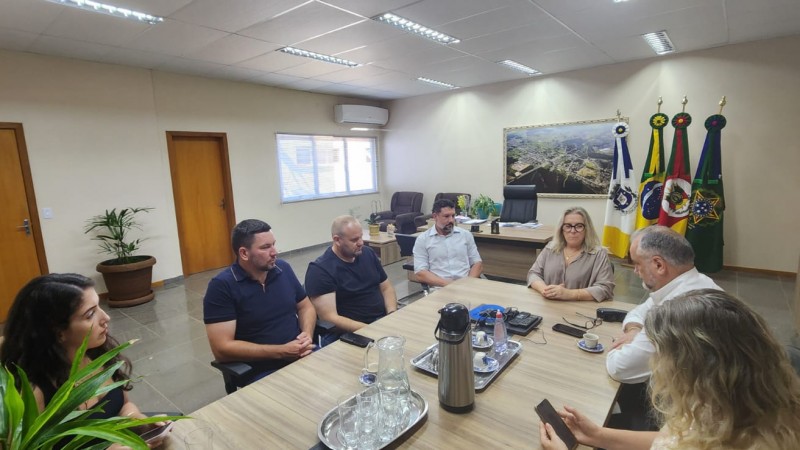 A imagem mostra a Presidente Baretta, a Prefeita de Minas do Leão, Silvia Lasek,  Vice-Prefeito Daniel Oliboni, acompanhados de sua equipe, em uma reunião. Todos estão sérios e em um ambiente de trabalho, com mesas e cadeiras. A atmosfera é de colaboração e diálogo, refletindo o fortalecimento de laços institucionais entre os participantes. 