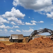  Uma paisagem com áreas de recuperação ambiental onde é depositada argila vermelha. O solo exibe tons intensos de vermelho, contrastando com o céu claro e azul ao fundo. A cena transmite a ideia de cuidado com o meio ambiente sendo cuidado