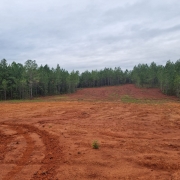 Área da Mina do Iruí em processo de recuperação ambiental. O solo é predominantemente vermelho, com aparência de argila recentemente colocada, característica de áreas em reabilitação após mineração de carvão. Há pouca vegetação visível, indicando a recomposição da cobertura vegetal.