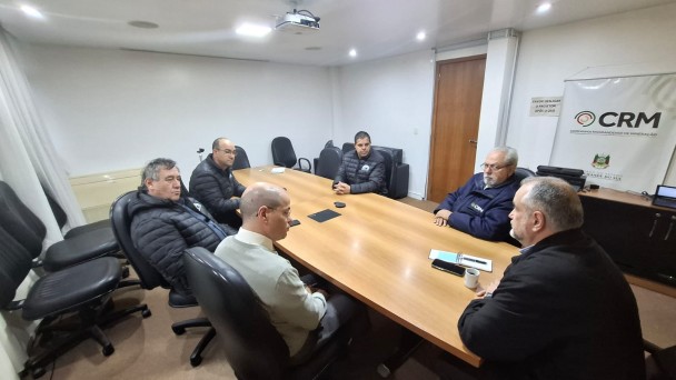 CRM em uma sala de reuniões. Todos estão sentados ao redor de uma mesa retangular, vestidos de forma formal ou com uniformes que remetem à atividade profissional. Os representantes sindicais demonstram expressão atenta e engajada, enquanto os diretores da CRM mantêm postura séria e profissional. 