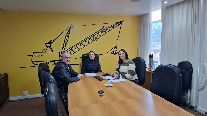 Três pessoas sorrindo durante uma reunião em um ambiente vibrante e amarelo, transmitindo uma atmosfera amigável e energizante.