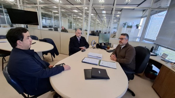 Tr&ecirc;s pessoas est&atilde;o reunidas em volta de uma mesa oval conversando profissionalmente e est&atilde;o bem atentas ao assunto acerca do bom funcionamento da Companhia.