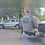 Na imaem mostra de costas um profissional vestido de PM da Briaa Militar e uma viatura &agrave; sua frente. 